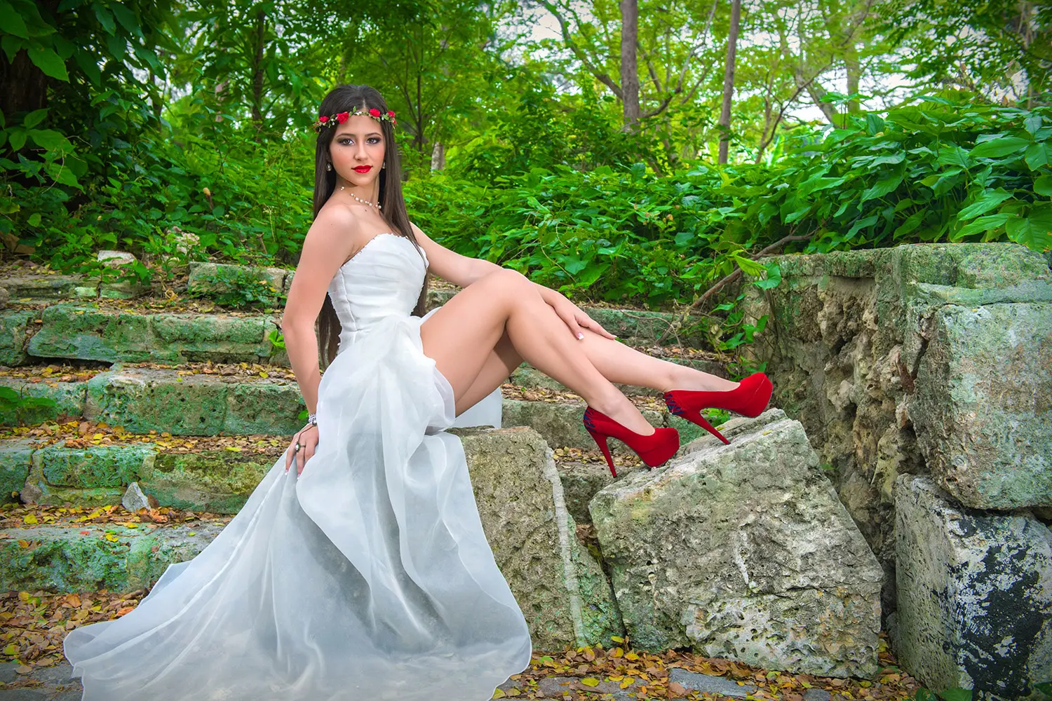 Joven de traje blanco posando sentada sobre piedras en el bosque
