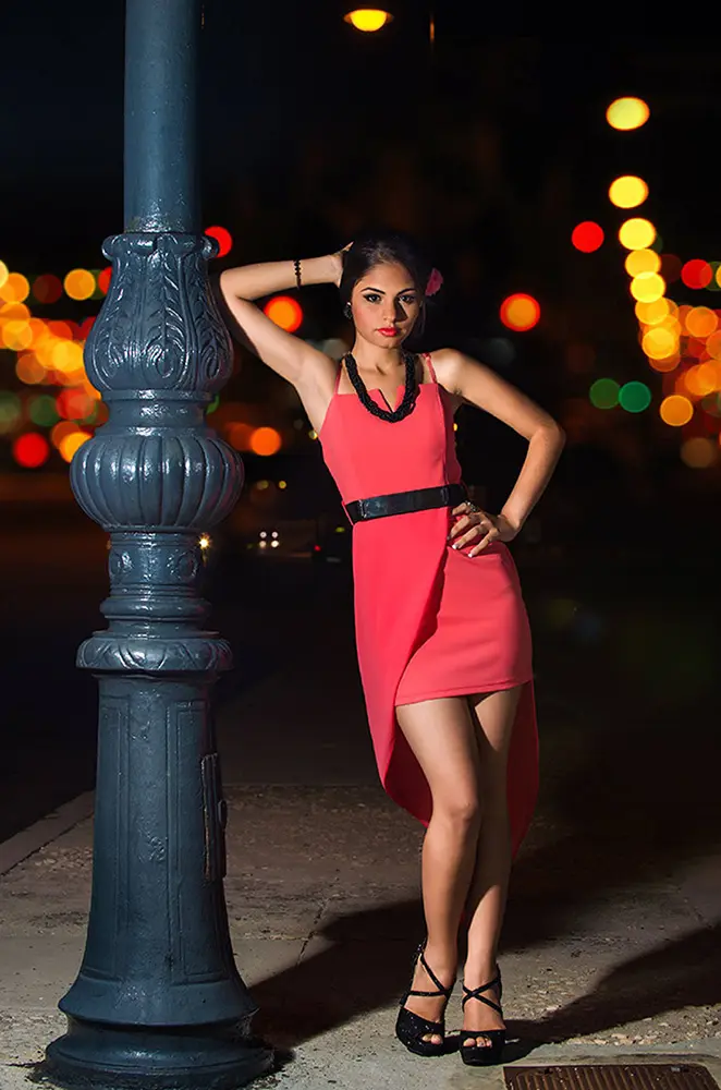 Muchacha recostada a farola en la calle en la noche con luces de la ciudad de fondo