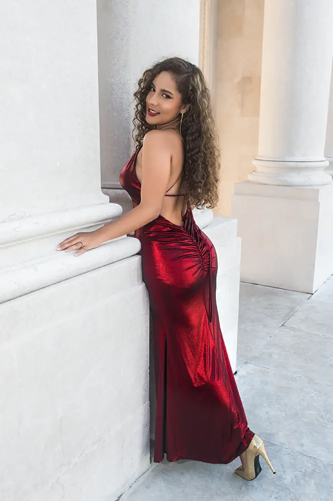 Chica de pelo rizo posando de lado frente a columnas antiguas