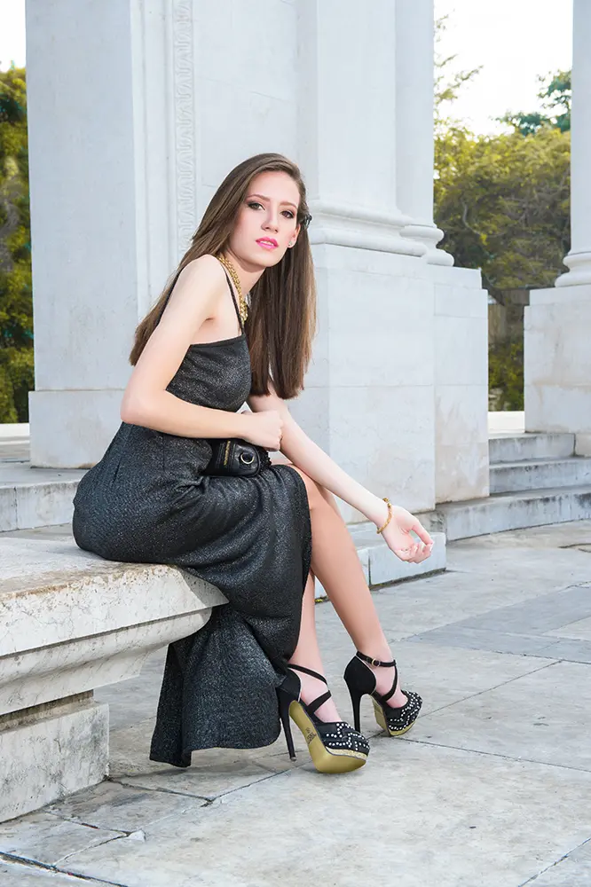 Modelo estilizada con vestido negro elegante sentada sobre banco de mármol
