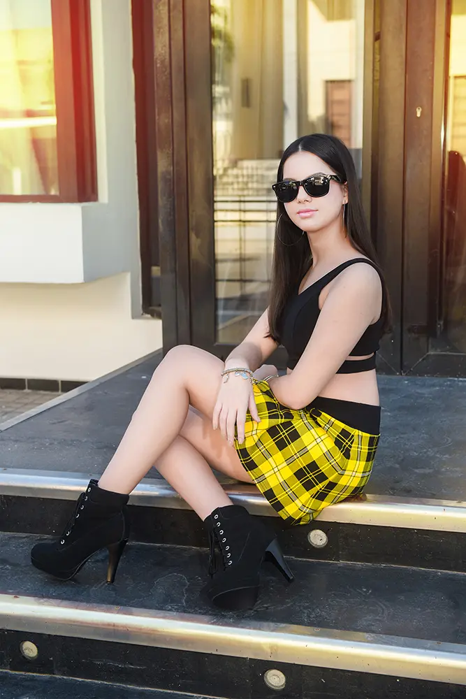 Jovencita con gafas de sol con saya corta a cuadros y top negro