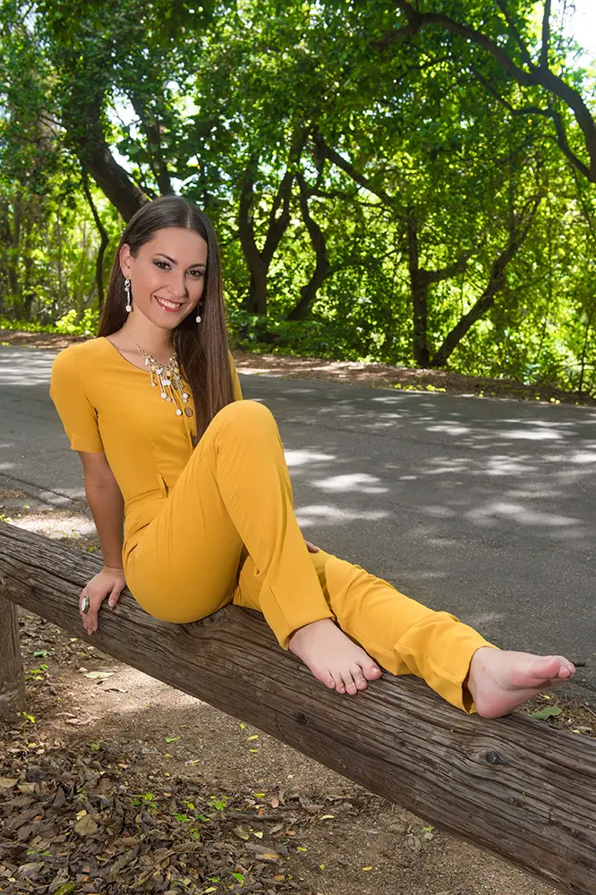 Modelo con ropa enteriza amarilla sentada sobre baranda de cerca en la naturaleza