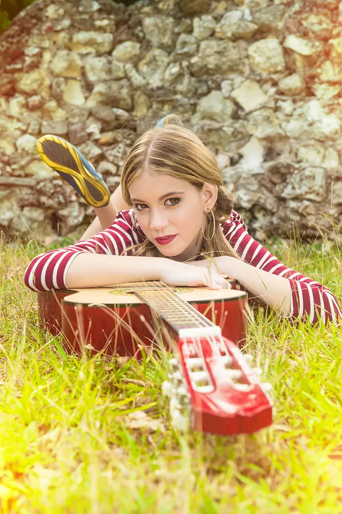Joven rubia con guitarra sobre la hierba verde